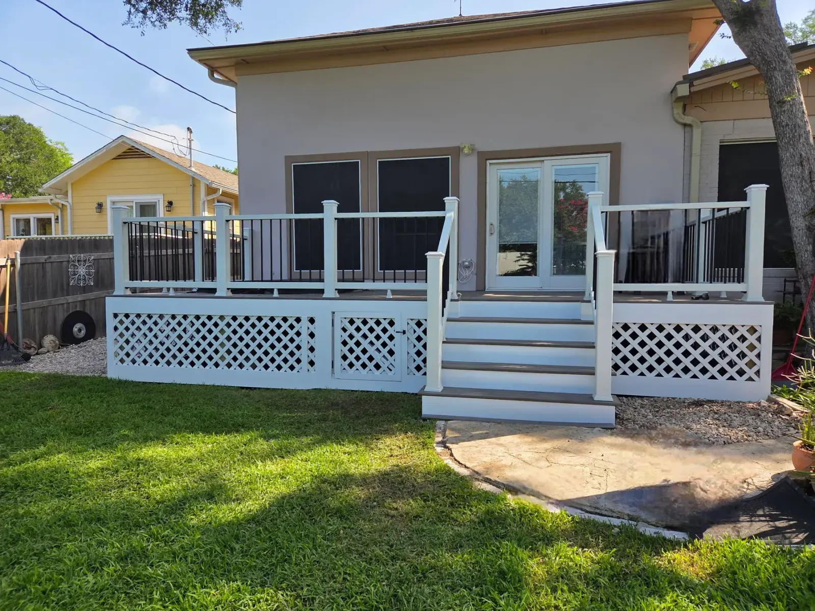 Finished residential backyard deck with white railings, black balusters, stairs, and lattice skirting