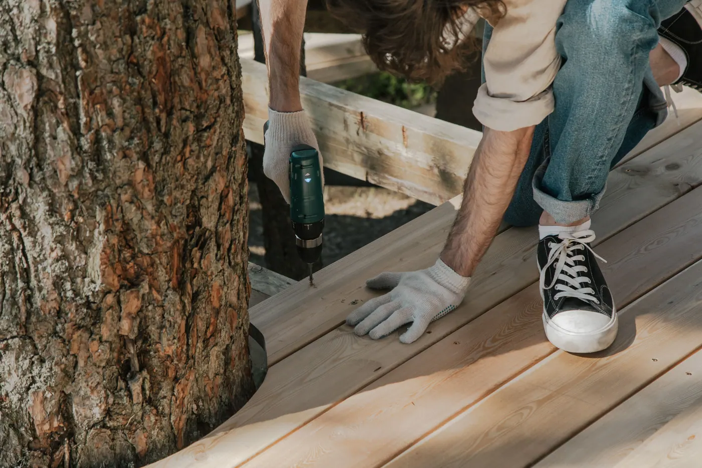 Worker fastening new deck boards with a drill during outdoor deck construction