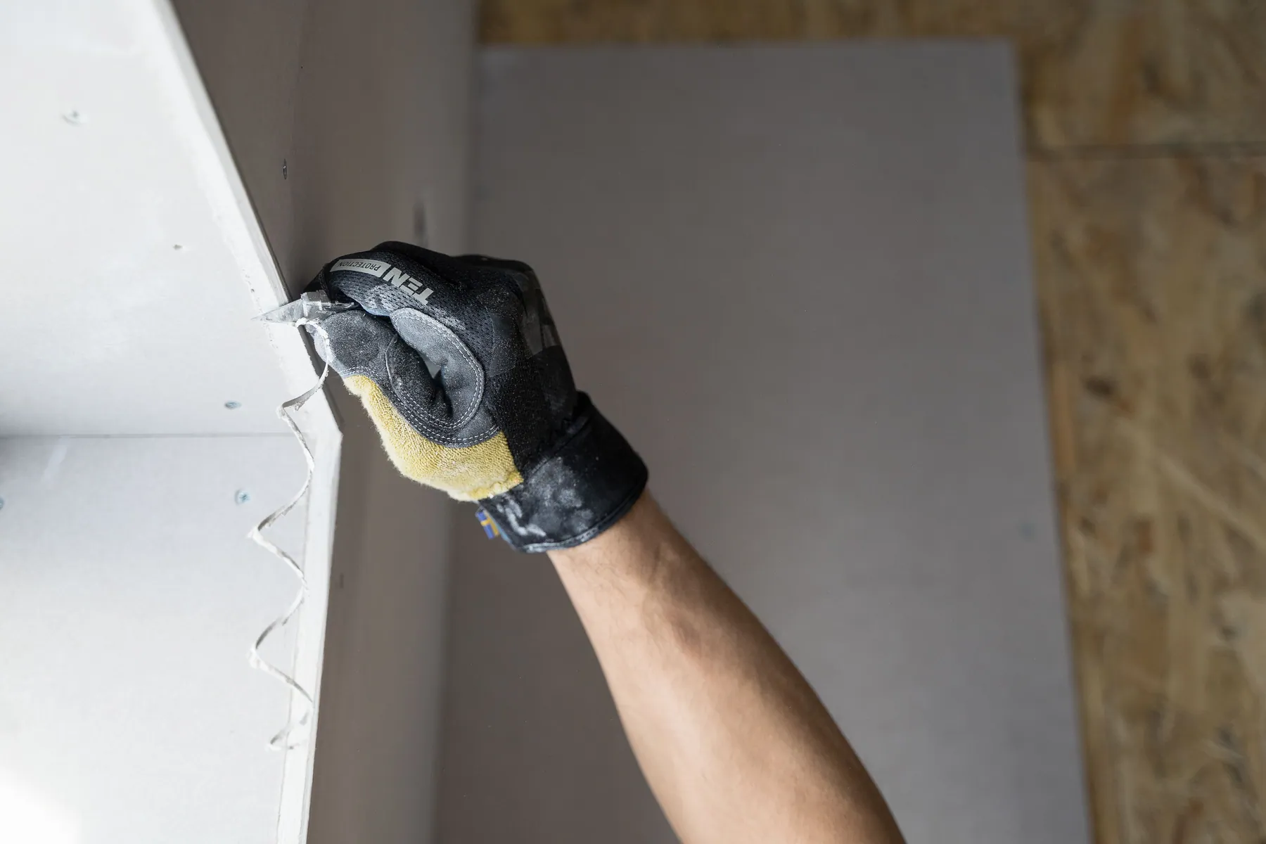 Gloved hand cutting and fitting a drywall panel during residential wall repair