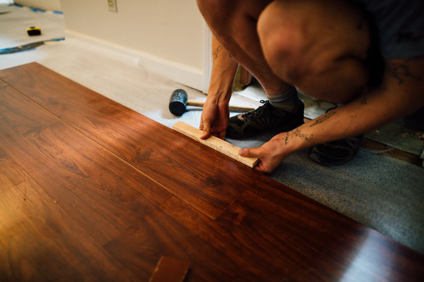 Installer fitting wood-look flooring at a room transition with flooring tools nearby
