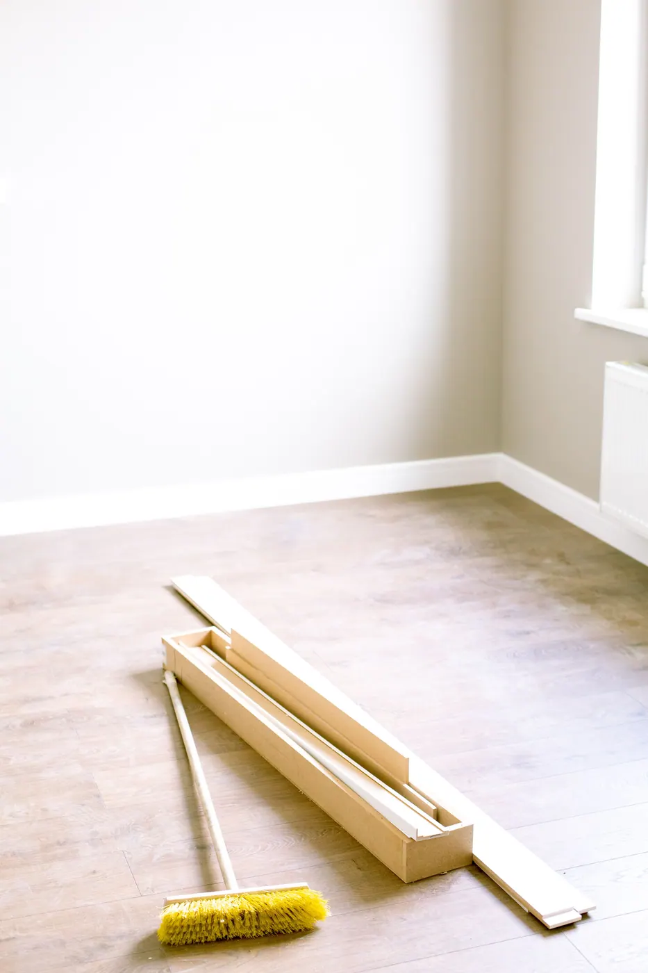 Room with new wood-look flooring, trim pieces, and a broom during installation