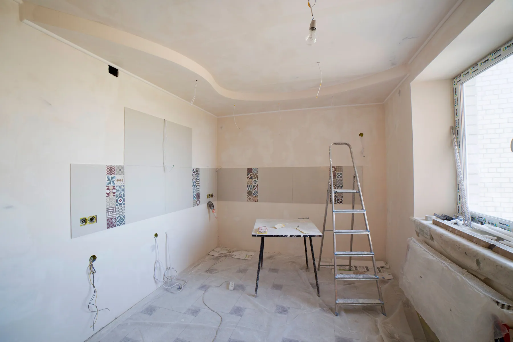Kitchen renovation in progress with ladder, tile work, and protected floors