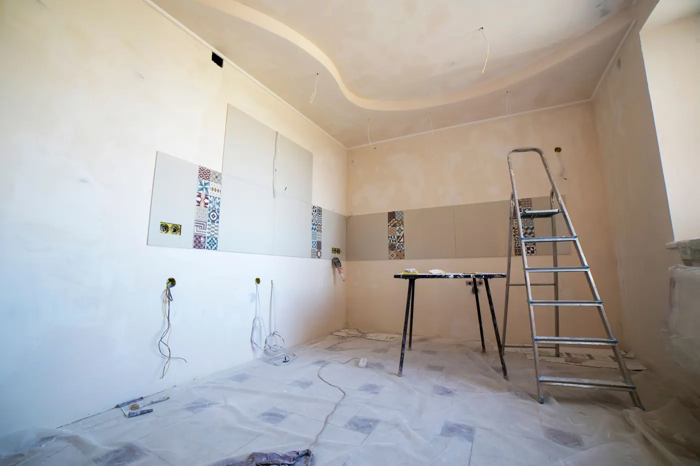 Room renovation in progress with ladder, protected floors, and finish materials