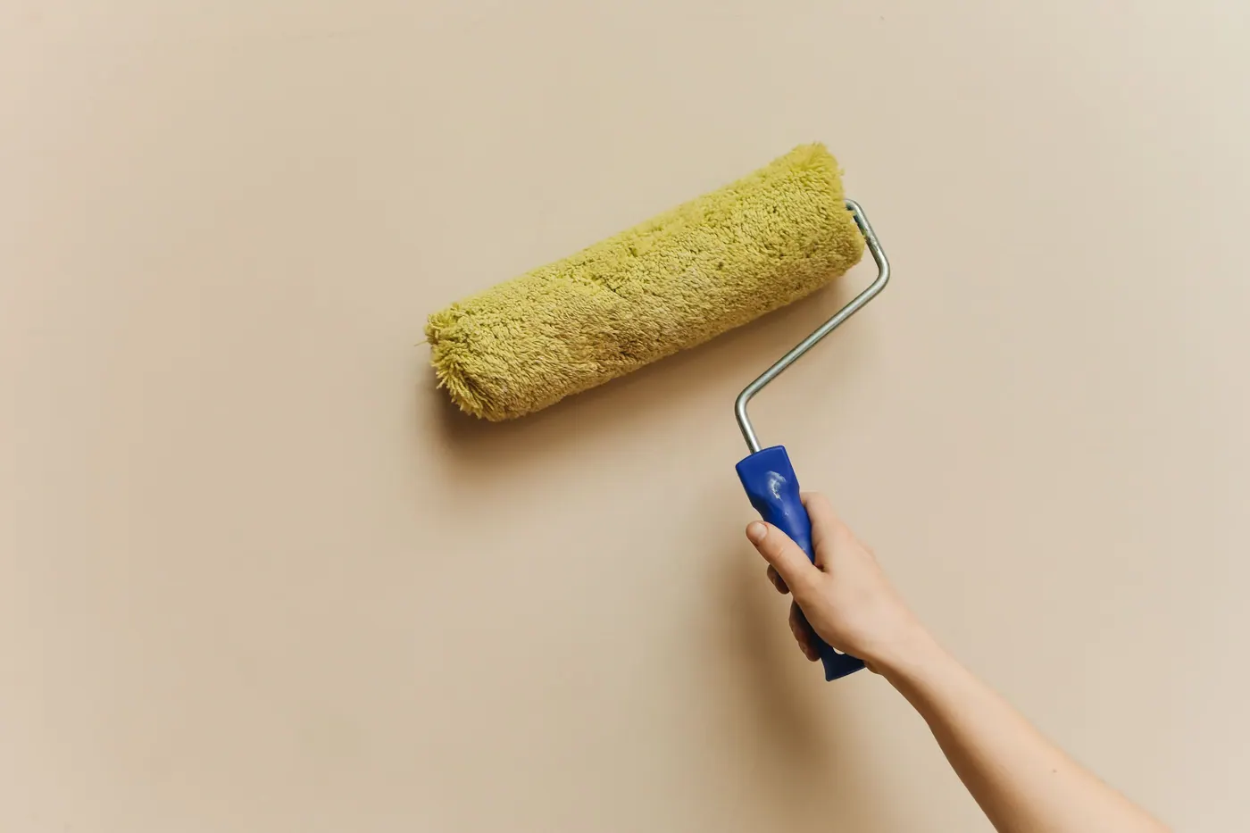 Hand using a roller to apply warm neutral paint to an interior wall