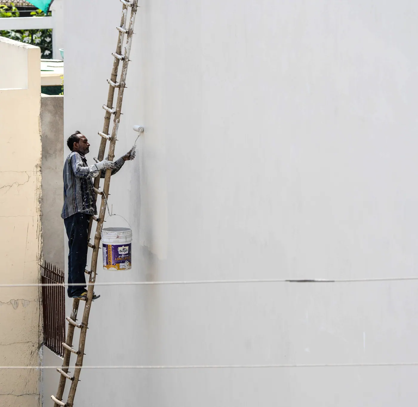 Exterior painter working from a ladder to roll fresh paint onto a wall